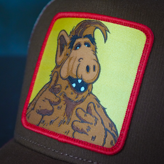 Close-up of a woven patch of ALF on yellow background attached to the crown.