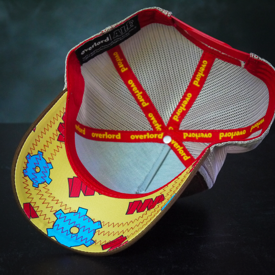 Inside view of brown twill trucker cap with gears and cogs printed on yellow underbrim.