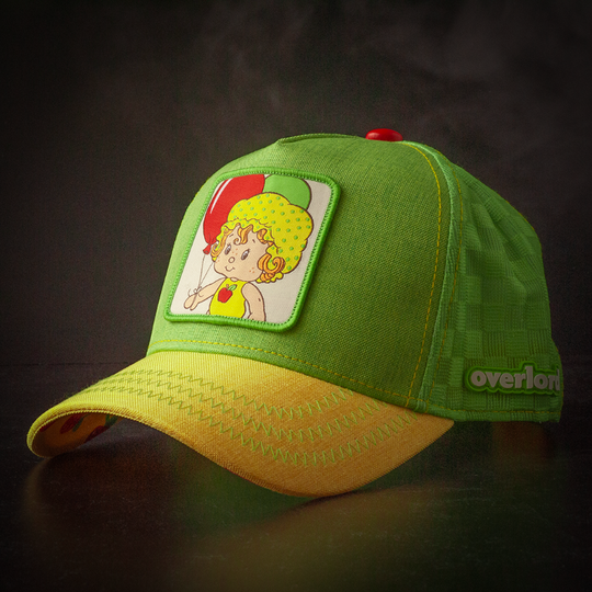 Green and yellow linen trucker cap hat featuring Apple Dumplin' from Strawberry Shortcake on square woven patch attached to crown against a black background