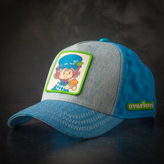Blue linen trucker cap hat featuring a woven patch on crown with Blueberry Muffin from Strawberry Shortcake against a black background