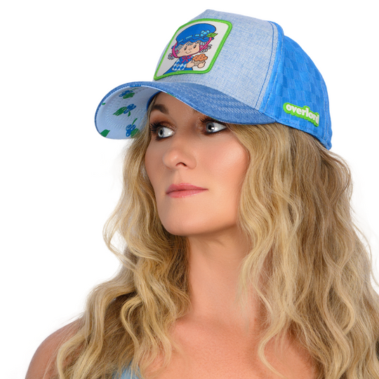 Woman wearing a blue linen trucker cap hat featuring a woven patch on crown with Blueberry Muffin from Strawberry Shortcake