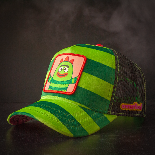 Plush green striped trucker cap hat featuring Brobe from Yo Gabba Gabba on woven patch attached to crown against black background