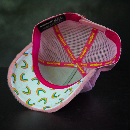 Inside view of pink faux fur trucker cap with rainbows printed on white underbrim.