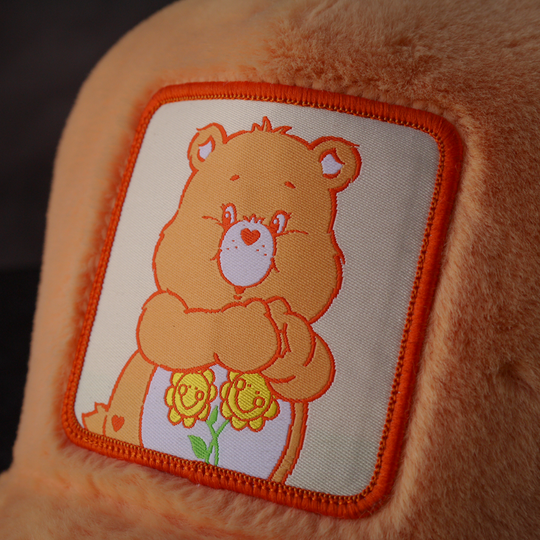 Close-up of a woven patch of Friendship Bear from Care Bears attached to the trucker cap crown.
