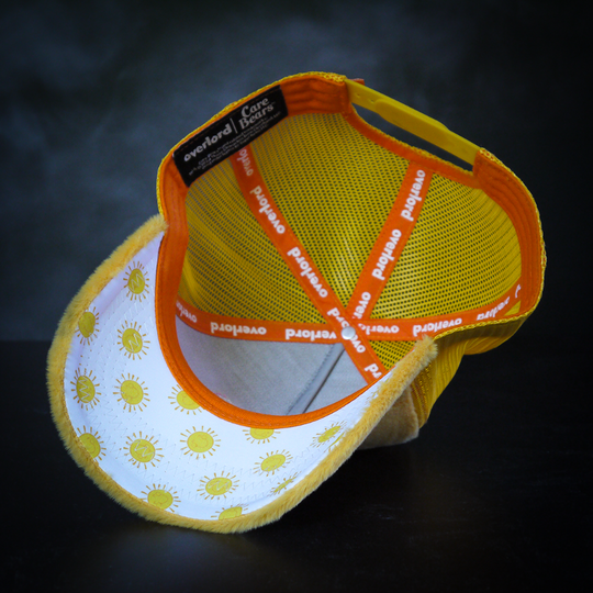 Inside of yellow faux fur trucker cap with yellow suns printed on white underbrim.