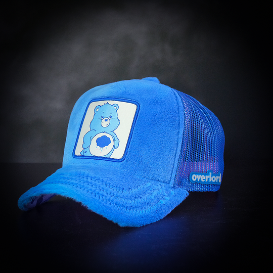 Blue faux fur trucker cap with blue mesh featuring a woven patch of Grumpy Bear from Care Bears attached to the crown.