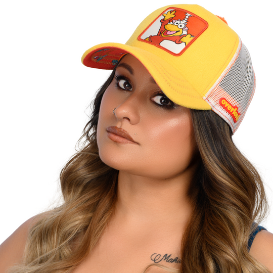 Woman wearing yellow fleece trucker cap hat with Fraggle Rock Red woven patch against white background