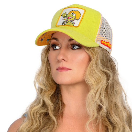 Woman wearing yellow fleece trucker cap hat with Fraggle Rock Wembley woven patch against white background