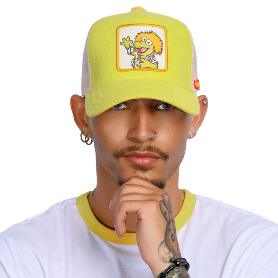 Man wearing yellow fleece trucker cap hat with Fraggle Rock Wembley woven patch against white background