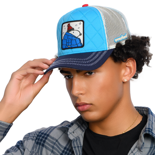 Man wearing a quilted blue trucker cap hat with Peanuts Snoopy in blue jacket woven patch against a white background