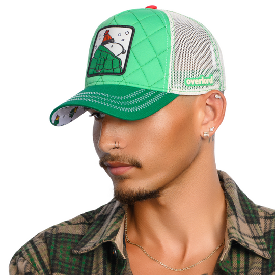 Man wearing quilted green trucker cap hat with Peanuts Snoopy in green jacket woven patch against a white background