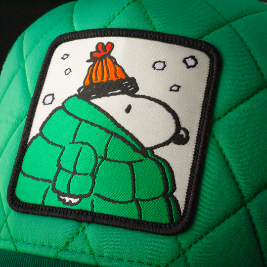 Close-up of Peanuts Snoopy in green jacket woven patch on quilted green trucker cap hat.