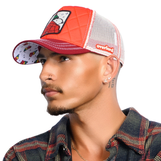 Man wearing quilted red trucker cap hat with Peanuts Snoopy in red jacket woven patch against a white background