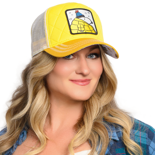 Woman wearing a quilted yellow trucker cap hat with Snoopy in Jacket woven patch against a white background