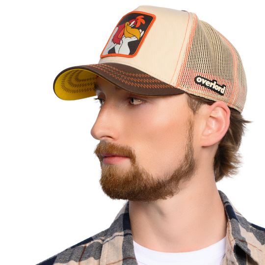 Man wearing a beige and brown trucker cap with Foghorn Leghorn patch on crown