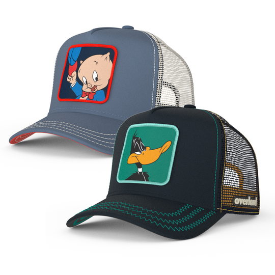 Two trucker hats featuring animated characters Daffy Duck and Porky Pig from Looney Tunes. One hat is gray with a red visor, and the other is black with a green visor, both have 'OVERLORD' branding.
