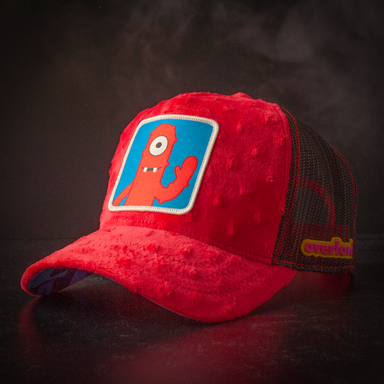Red plush minky trucker cap hat featuring Muno from Yo Gabba Gabba on woven patch attached to crown against black background
