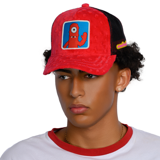 Man wearing red plush minky trucker cap hat featuring Muno from Yo Gabba Gabba on woven patch attached to crown