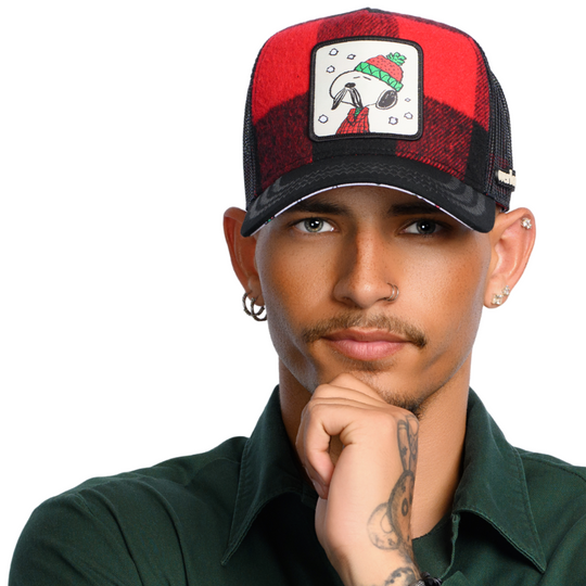 Man wearing red and black buffalo plaid flannel trucker cap with black mesh featuring a woven patch of Lumberjack Snoopy from the Peanuts attached to the crown.