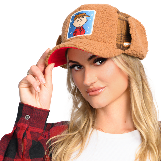 Woman wearing a brown Sherpa cap, with brown Sherpa ear-flaps, and woven patch of Charlie Brown on the front
