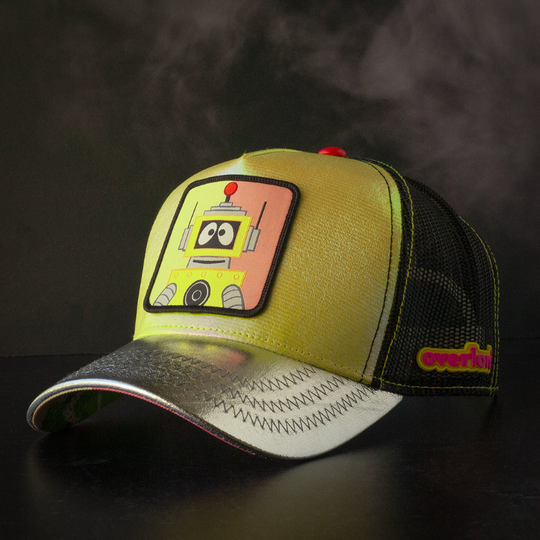 Metallic yellow and silver trucker cap hat featuring Plex from Yo Gabba Gabba on woven patch attached to crown against black background