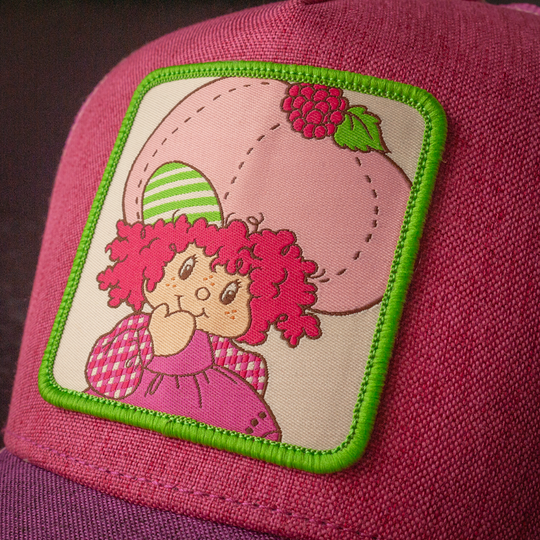 Close-up of Strawberry Shortcake Raspberry Tart woven patch on magenta linen trucker cap hat
