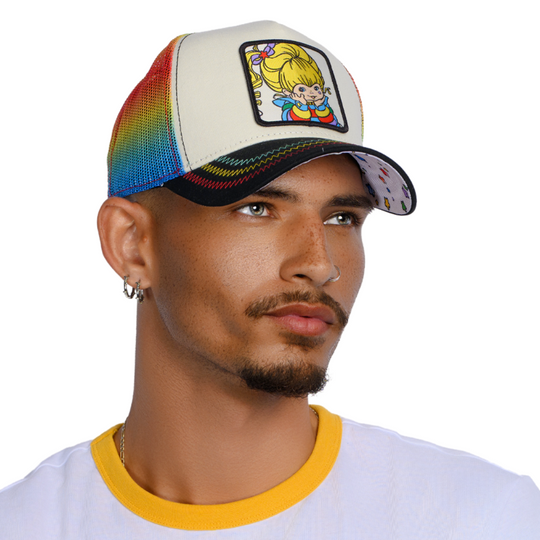 Man wearing black and white trucker cap hat with rainbow mesh featuring Rainbow Brite on woven patch attached to crown