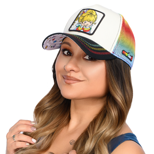 Woman wearing a black and white trucker cap hat with rainbow mesh featuring Rainbow Brite on woven patch attached to crown