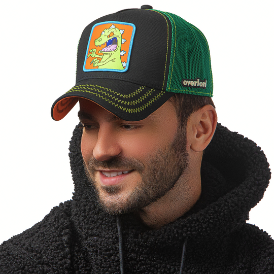 Man wearing black OVERLORD X Rugrats Reptar trucker baseball cap hat with green zig zag stitching. PVC Overlord logo.