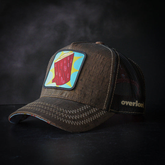 Brown cork wood trucker cap hat featuring Log from Ren and Stimpy on woven patch attached to crown against black background