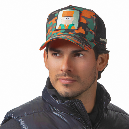 Man wearing orange, green, black and brown trucker cap with black mesh featuring a woven patch featuring Jimbo Kern from South Park attached to the crown.