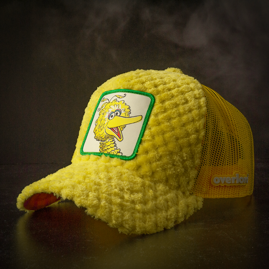 Yellow faux fur trucker cap hat featuring Big Bird from Sesame Street on woven patch attached to crown against black background