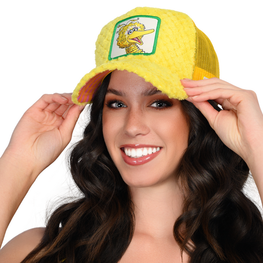 Woman wearing yellow faux fur trucker cap hat featuring Big Bird from Sesame Street on woven patch attached to crown