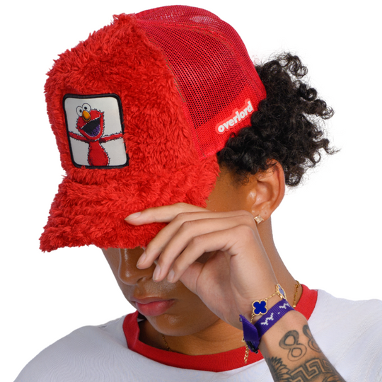 Man wearing red faux fur trucker cap hat featuring Elmo from Sesame Street on woven patch attached to crown