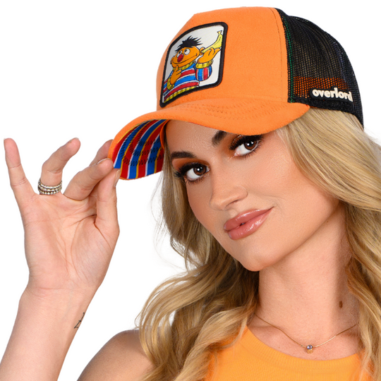 Woman wearing orange fleece trucker cap hat with Sesame Street Ernie woven patch against a white background