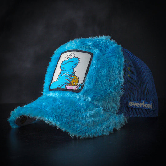 Turquoise faux fur trucker cap hat featuring Cookie Monster from Sesame Street on woven patch attached to crown against black background