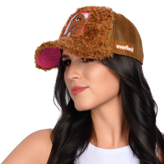 Woman wearing brown faux fur trucker cap hat with Sesame Street Snuffleupagus woven patch against white background