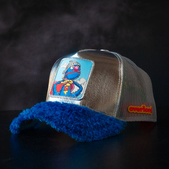 Metallic silver and blue faux fur trucker cap hat featuring Super Grover from Sesame Street on woven patch attached to crown against black background