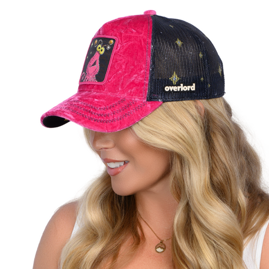 Woman wearing hot pink crushed velvet trucker cap hat with Sesame Street pink yip martian woven patch against white background