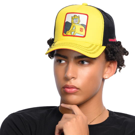 Man wearing yellow trucker cap hat featuring Bumblebee from Transformers on woven patch attached to crown