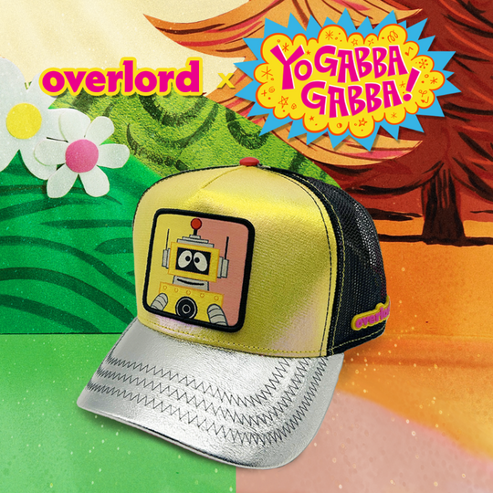 Metallic yellow and silver trucker cap hat featuring Plex from Yo Gabba Gabba on woven patch attached to crown against Plex's world.