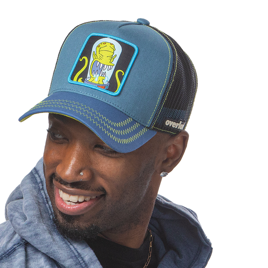 Man wearing blue OVERLORD X The Simpsons present Kodos the alien trucker baseball cap hat with lime green zig zag stitching. PVC Overlord logo.