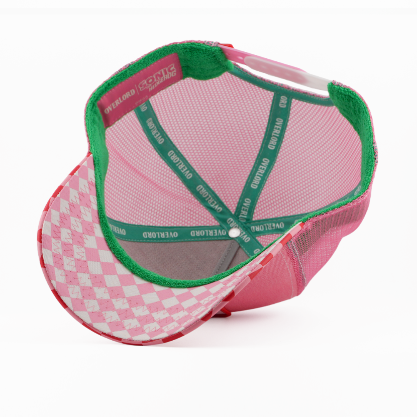 Underside of the Amy Rose from Sonic the Hedgehog retro trucker cap, showing a pink and white argyle-pattern brim, Sonic the Hedgehog tag, pink mesh crown, and green Overlord branded taping with white text.