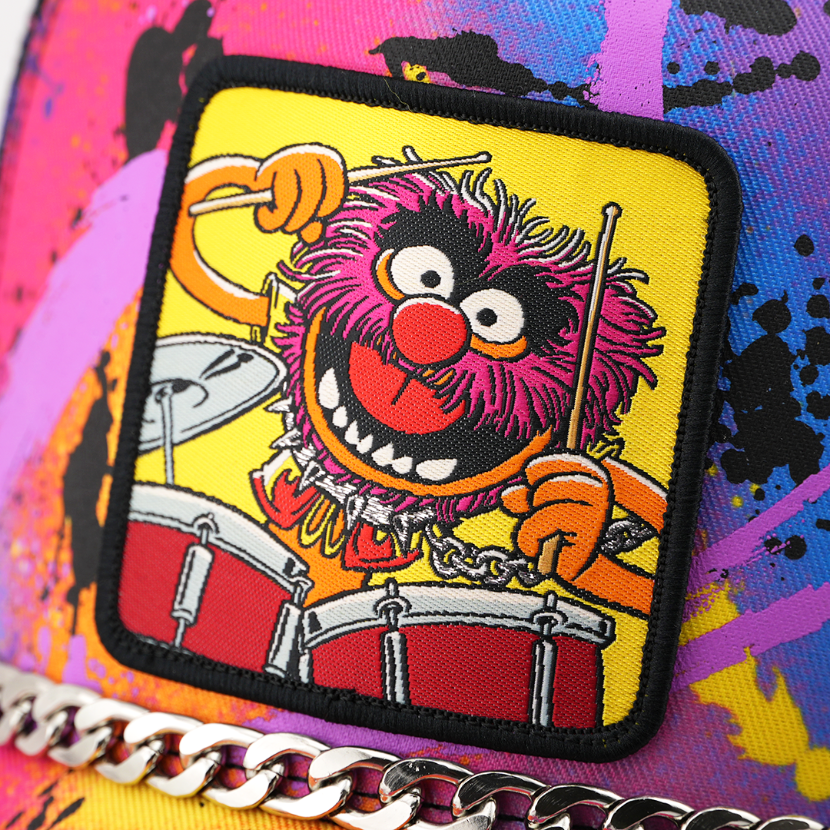 A close-up of a colorful patch featuring the Muppet character Animal playing drums, attached to a bright multicolor surface with paint-splatter style graphics and a silver chain detail.