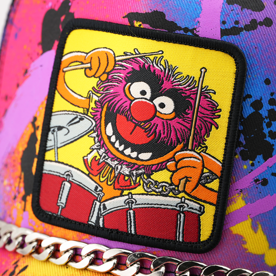 A close-up of a colorful patch featuring the Muppet character Animal playing drums, attached to a bright multicolor surface with paint-splatter style graphics and a silver chain detail.