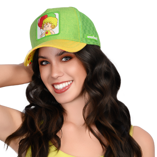 Woman wearing green and yellow linen trucker cap hat featuring Apple Dumplin' from Strawberry Shortcake on square woven patch attached to crown.