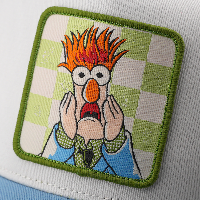 Close-up of a woven patch showing Beaker from The Muppets with wide eyes and hands raised to his face on a green checkered background, stitched onto white fabric with a green border.