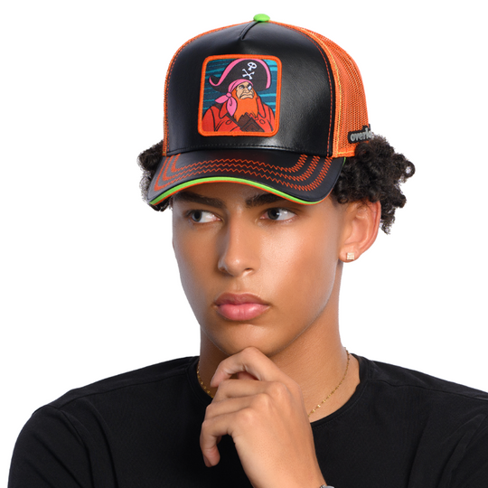 Man wearing black faux leather trucker cap with orange mesh featuring a woven patch of Red Beard villain from Scooby Doo attached to the crown.