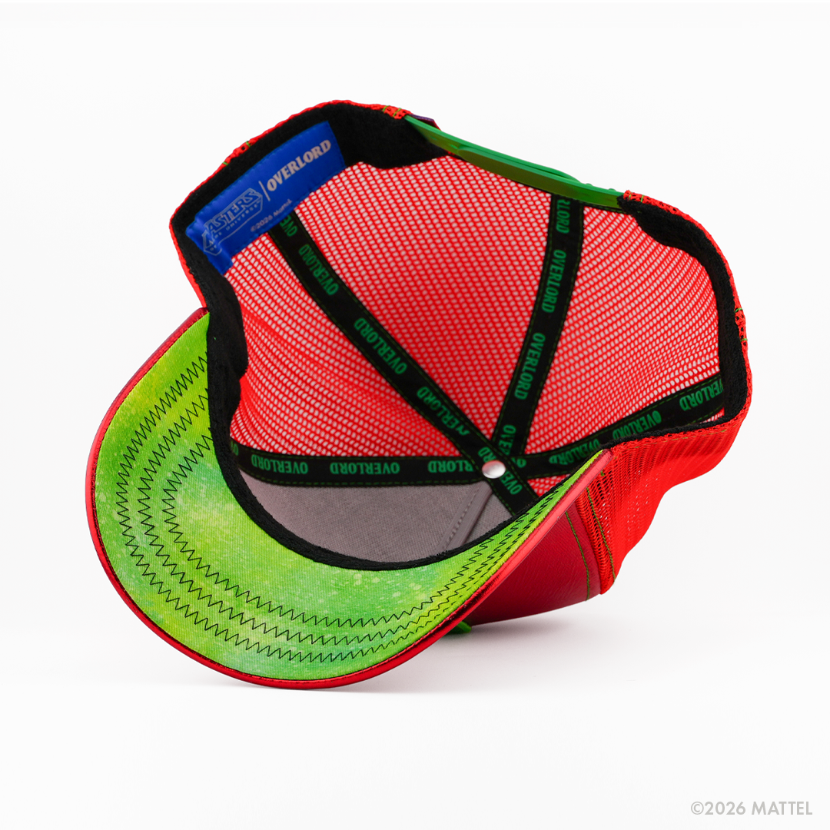 Underside of the Beast Man from Masters of the Universe retro trucker cap, showing a green weathered-texture brim, blue Masters of the Universe tag, red mesh crown, and black Overlord branded taping with green text.