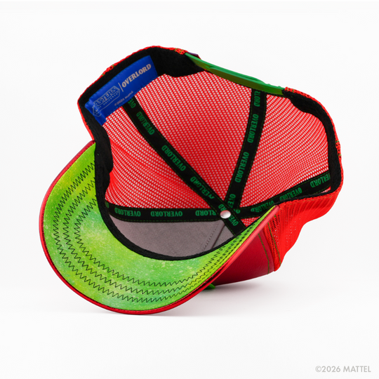 Underside of the Beast Man from Masters of the Universe retro trucker cap, showing a green weathered-texture brim, blue Masters of the Universe tag, red mesh crown, and black Overlord branded taping with green text.